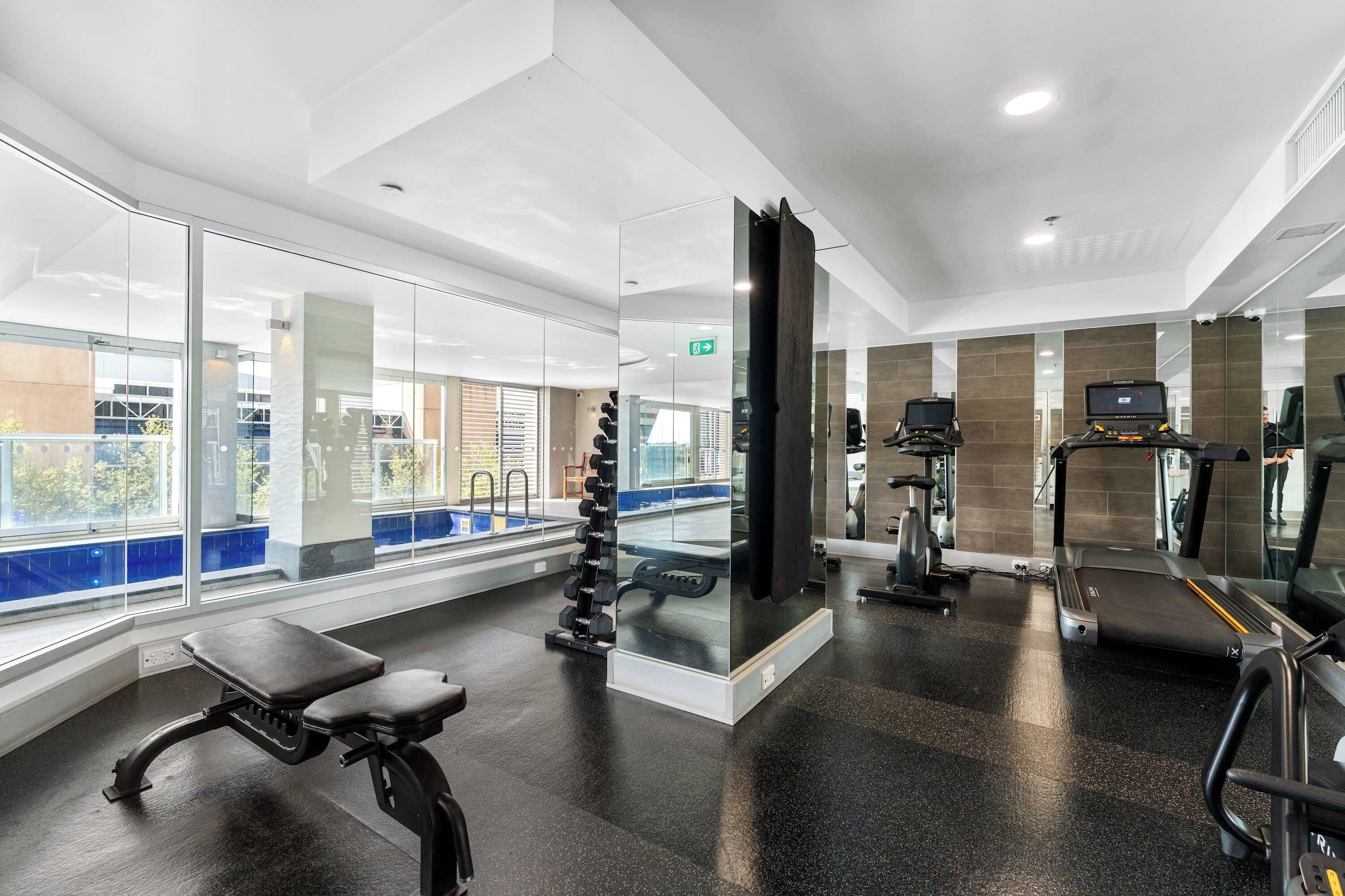 Un gimnasio moderno con equipo de ejercicio, una banca y vistas al exterior.