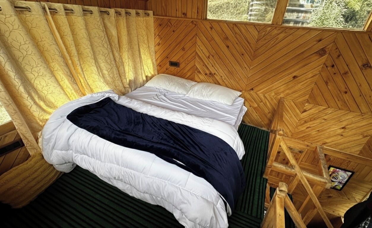 A wooden cabin room with a bed, a window, and a view of the outdoors.
