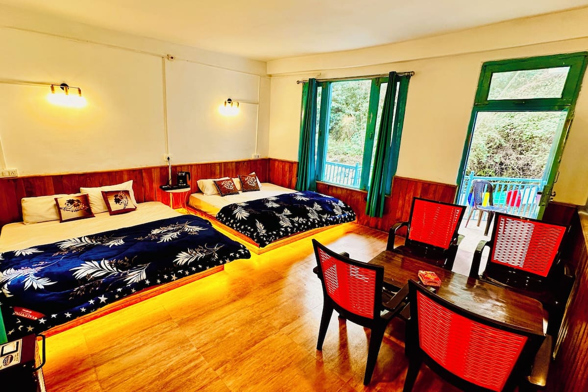 A room with two beds, a dining table, and chairs. There are two wall-mounted lights and a window with curtains.