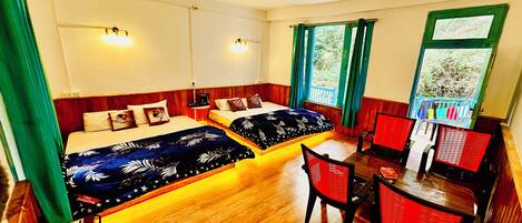 A room with two beds, a dining table, and chairs. There are two wall-mounted lights and a window with curtains.