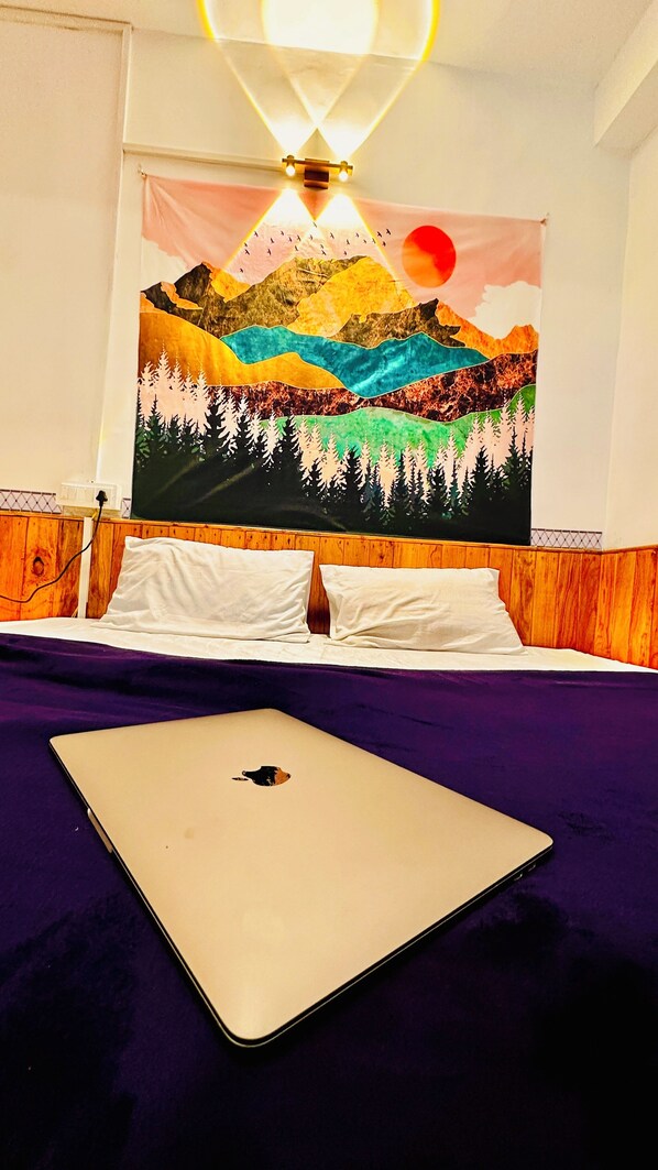 Un lit avec un ordinateur portable, une tête de lit en bois et une tapisserie représentant un paysage de montagne.
