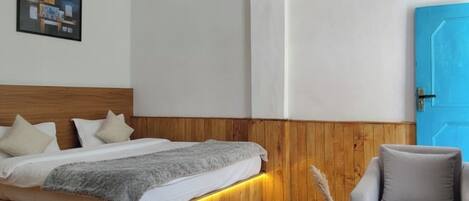 A modern hotel room with a wooden headboard, a bed with a gray blanket, a small table with a vase, and a blue door.