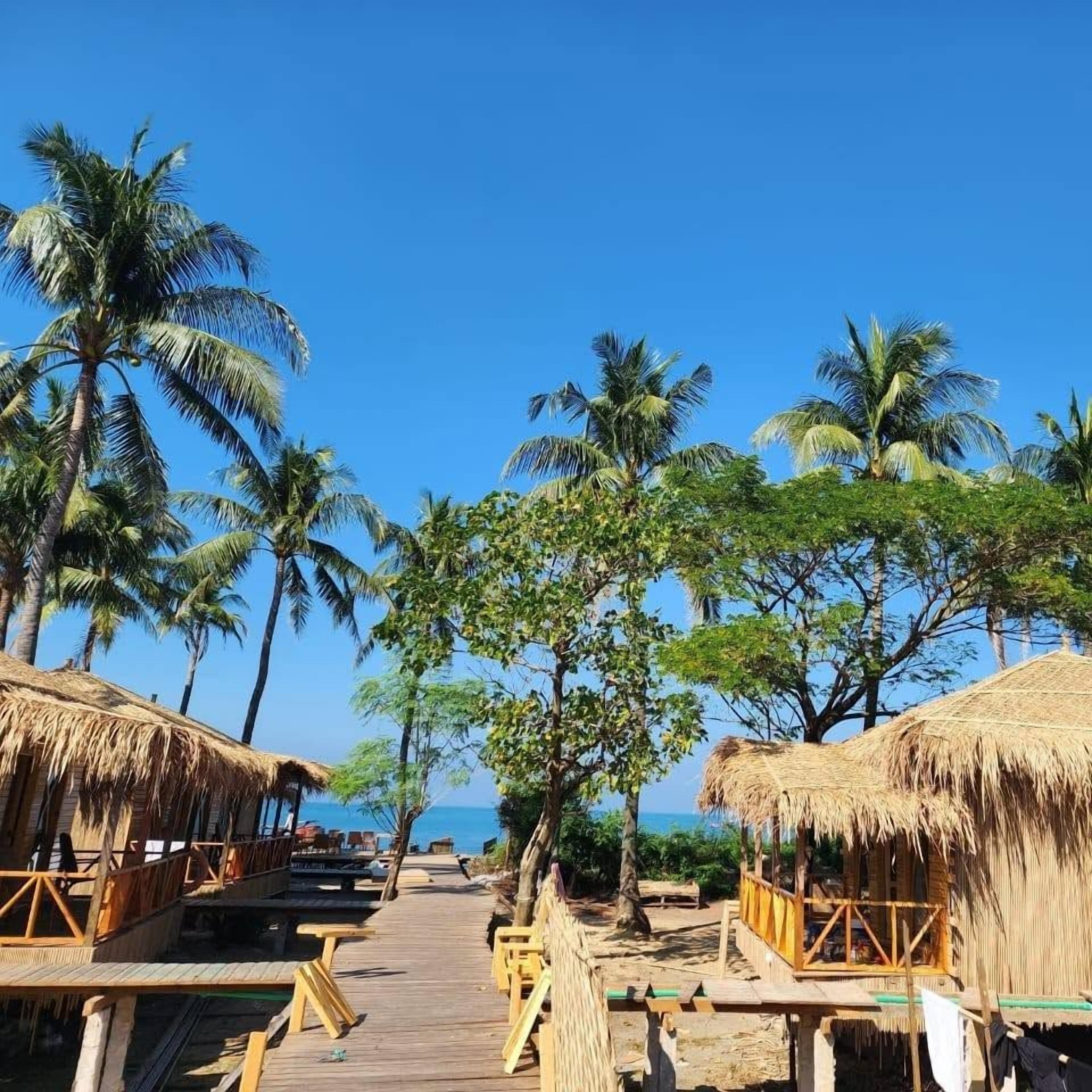 Eine hölzerne Steg, der zu überwasser Bungalows mit Strohdächern führt, umgeben von Palmen.