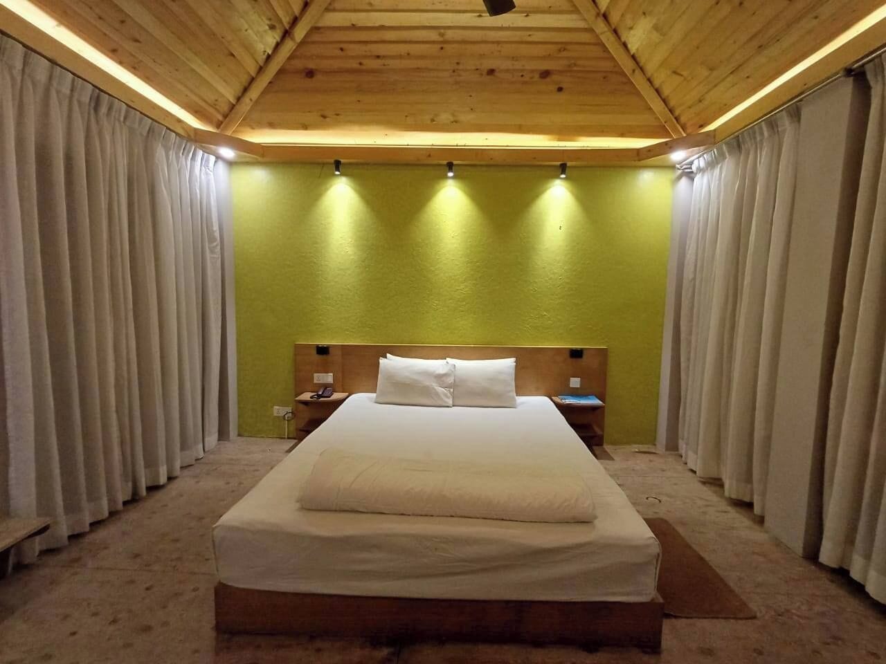 Un dormitorio con techo de madera, cama con ropa blanca, paredes verdes y cortinas a ambos lados.