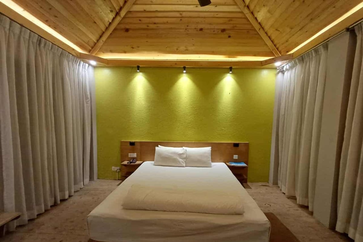 Ein Hotelzimmer mit Holzboden, einem Bett mit weißer Bettwäsche, einem Nachttisch und Vorhängen.
