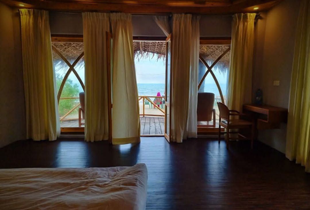 Ein Zimmer mit einem Bett, einem Schreibtisch und Blick auf das Meer durch große Fenster.