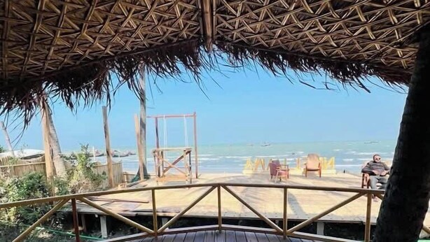 A wooden deck with a thatched roof, overlooking a beach with a clear view of the ocean and distant boats. - Neel Hawa Beach resort Saint Martin (Saint Martin's Island)