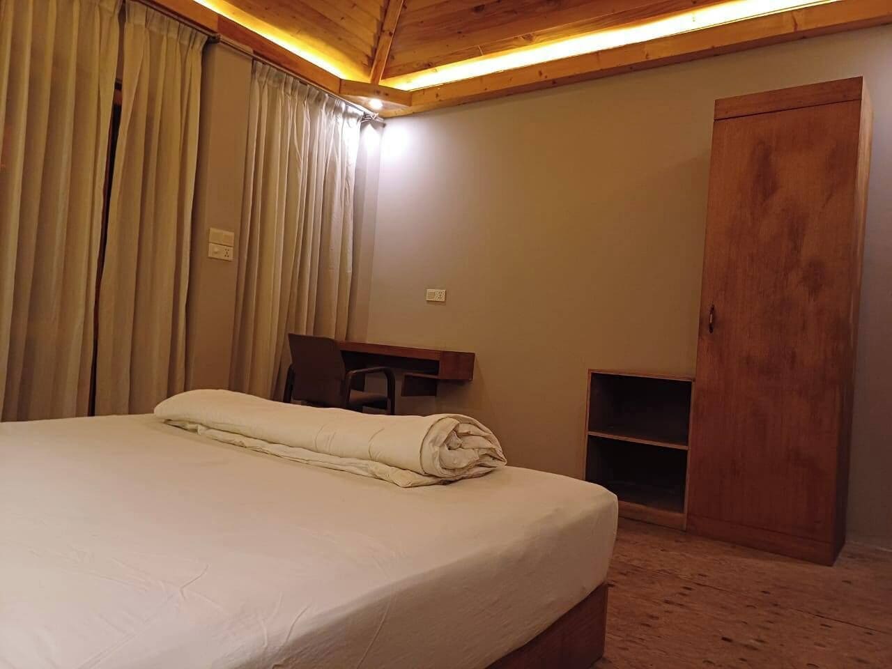 A hotel room with a bed, a desk, a wardrobe, and a small seating area.