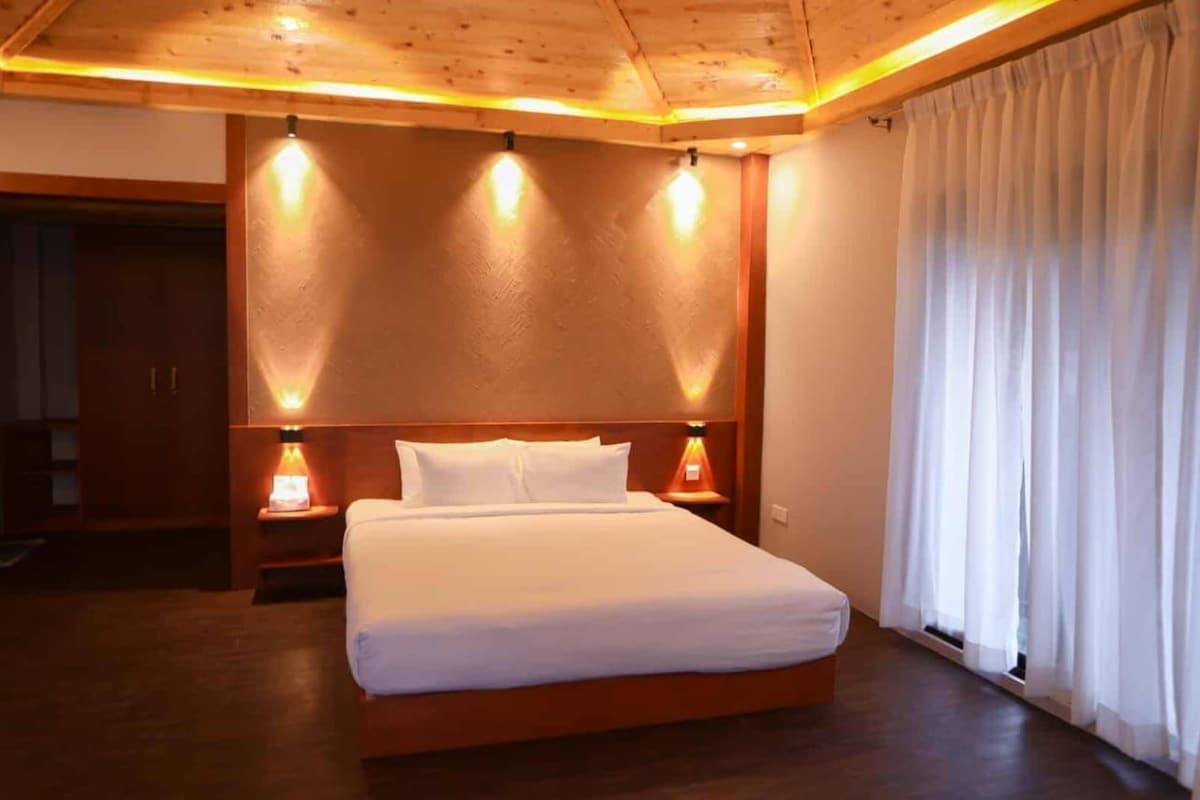 Ein Hotelzimmer mit Holzboden, einem Bett mit weißer Bettwäsche, zwei Nachttischlampen und einem Fenster mit Vorhängen.