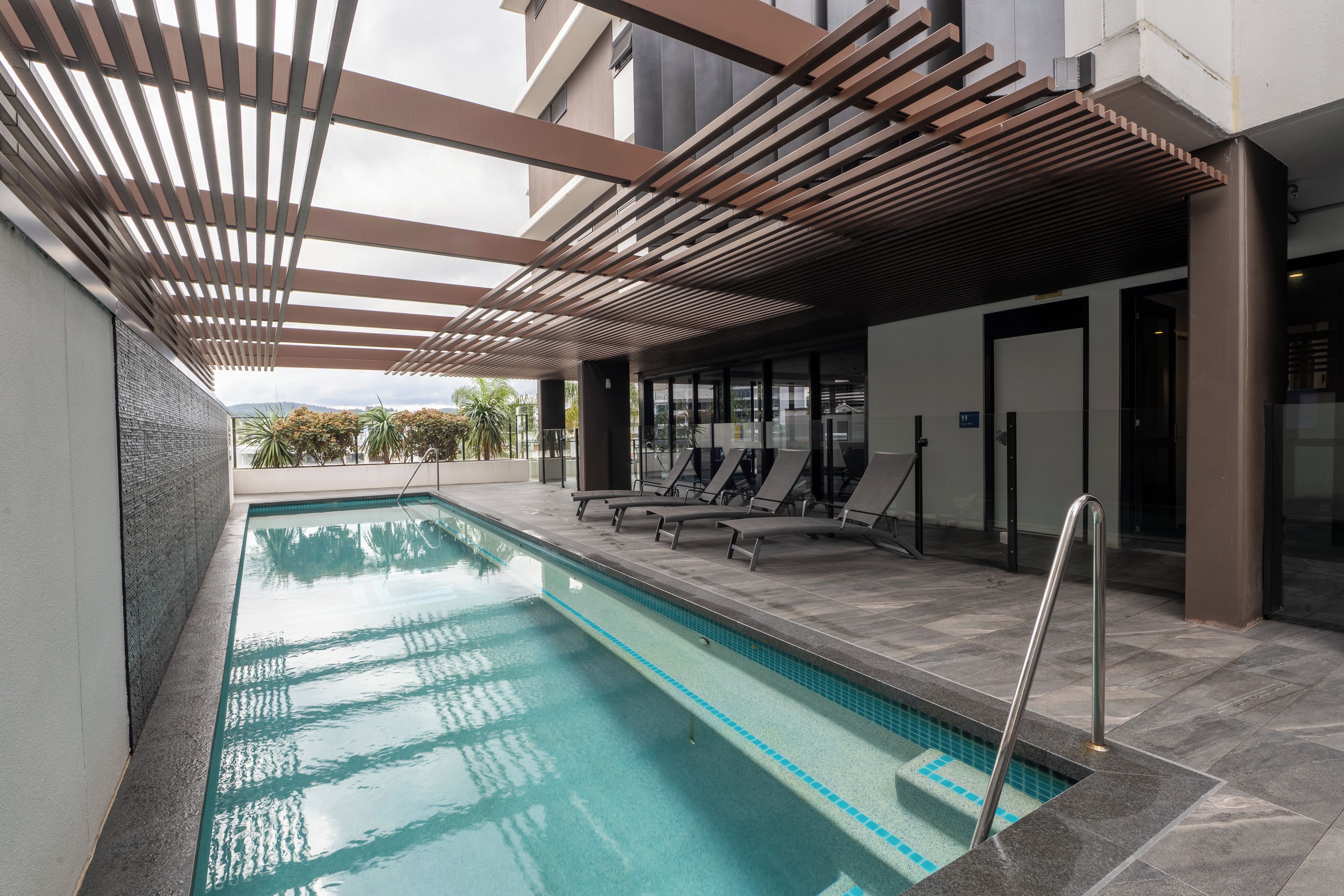 A swimming pool with a pergola overhead, lounge chairs, and a view of the surrounding area.
