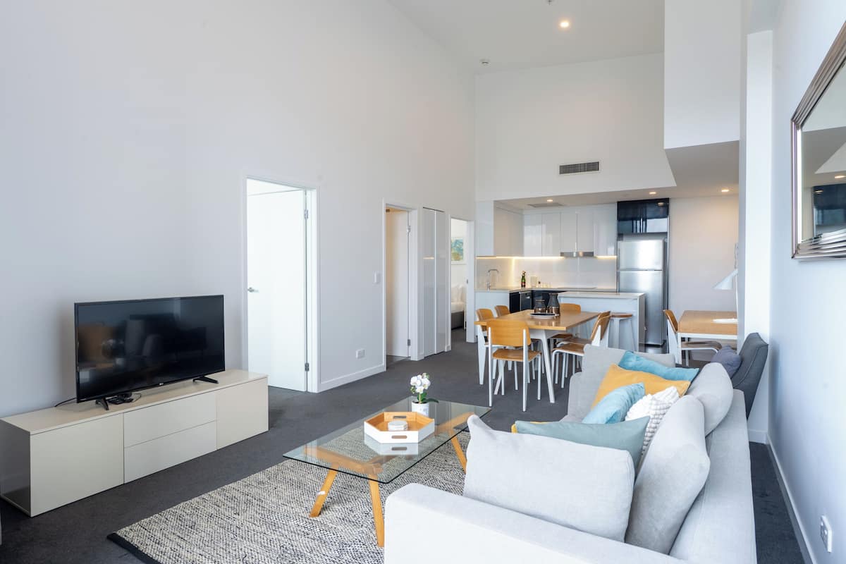 A modern living room with a flat-screen TV, a sofa, a coffee table, and a dining area with chairs and a table.
