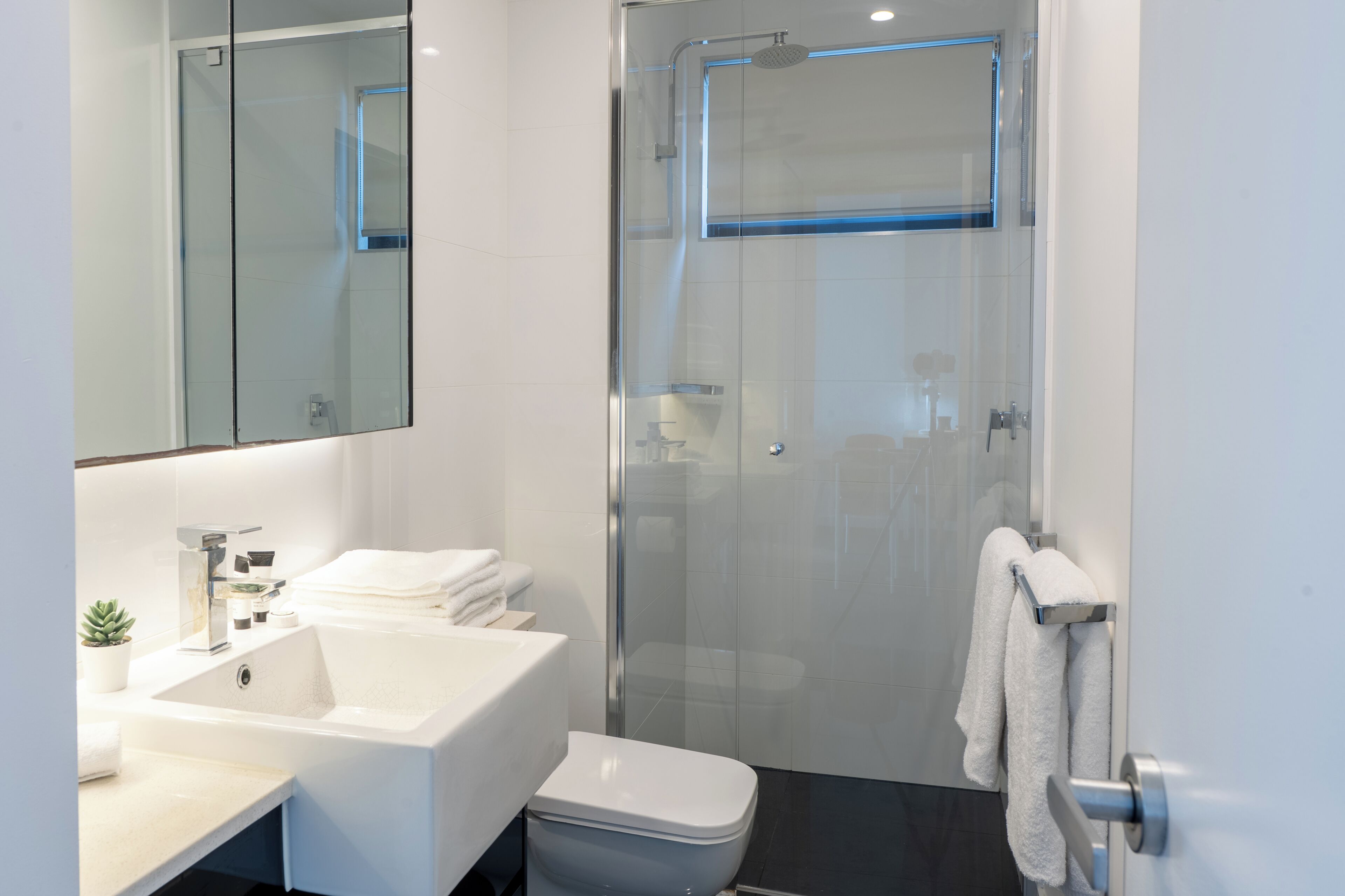 Un baño moderno con ducha de vidrio, lavamanos blanco y retrete.