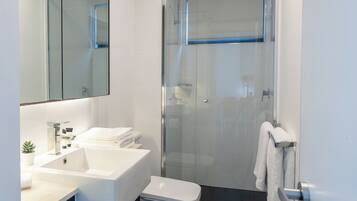Un baño moderno con ducha de vidrio, lavamanos blanco y retrete.