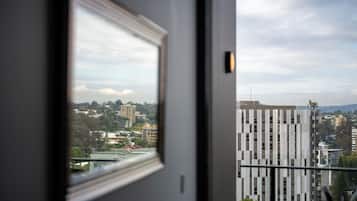 A view through a window of a building with a balcony, a cityscape with various buildings, and a partly cloudy sky.