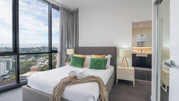 Una camera d'hotel moderna con un letto grande, vista sulla città, bagno con specchio e un comodino.