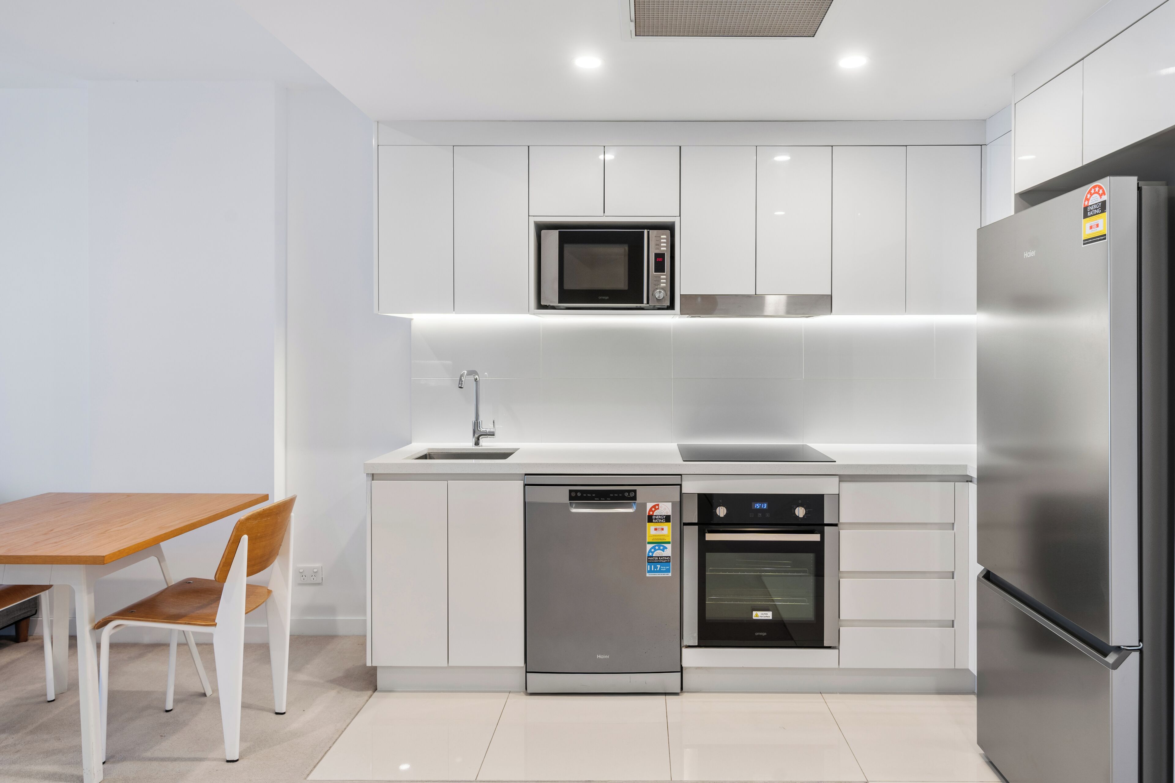 A modern kitchen with white cabinets, a microwave, a dishwasher, an oven, and a refrigerator.