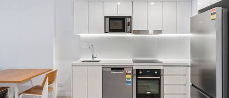 A modern kitchen with white cabinets, a microwave, a dishwasher, an oven, and a refrigerator.