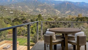 A terrace with a round table and chairs, overlooking a mountainous landscape.