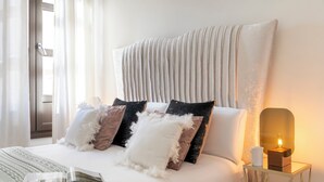 Ein ordentlich bezogenes Bett mit weiß-braunen Kissen, ein Nachttisch mit Lampe und eine Zeitschrift auf dem Bett.