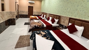 A hotel room with four beds arranged in a row, each with a red and white bedspread and matching pillows. The room has a marble floor and a green patterned wall. - Hotel Raghav Dham (Vrindavan)