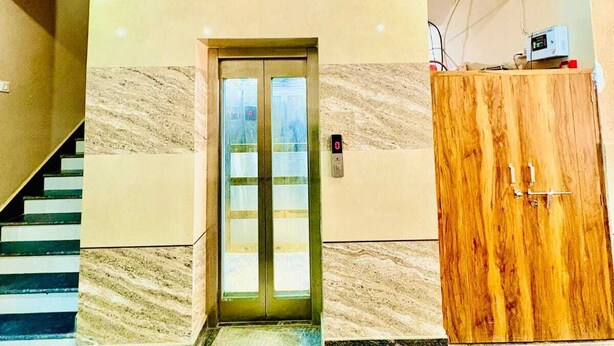 A lobby with a marble floor, a wooden cabinet, and a double door elevator. - Hotel Raghav Dham (Vrindavan)
