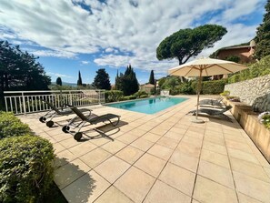 Ein Schwimmbecken mit Liegestühlen und einer Pergola, umgeben von Steinmauern und Grünpflanzen.