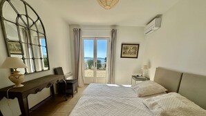 Quarto com cama, escrivaninha, cadeira, janela com cortinas e um quadro na parede.