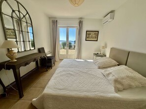 Ein Schlafzimmer mit einem Bett, einem Schreibtisch, einem Stuhl, einem Fenster mit Vorhängen und einem Bild an der Wand.