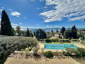 Ein Pool mit Blick auf das Meer, umgeben von Grünpflanzen und Bäumen.