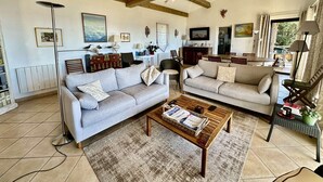 Uma sala de estar ampla com dois sofás, uma mesa de centro e um espaço para refeições com mesa e cadeiras.