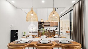 A modern dining area with a wooden table set for six, two pendant lights, and a kitchen in the background. - Sadin Villa by Kozystay - Sanur (Kerobokan)