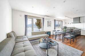 A modern living room with a sofa, a glass coffee table, and a dining area with chairs. - STELLAVIA (Nakafurano)