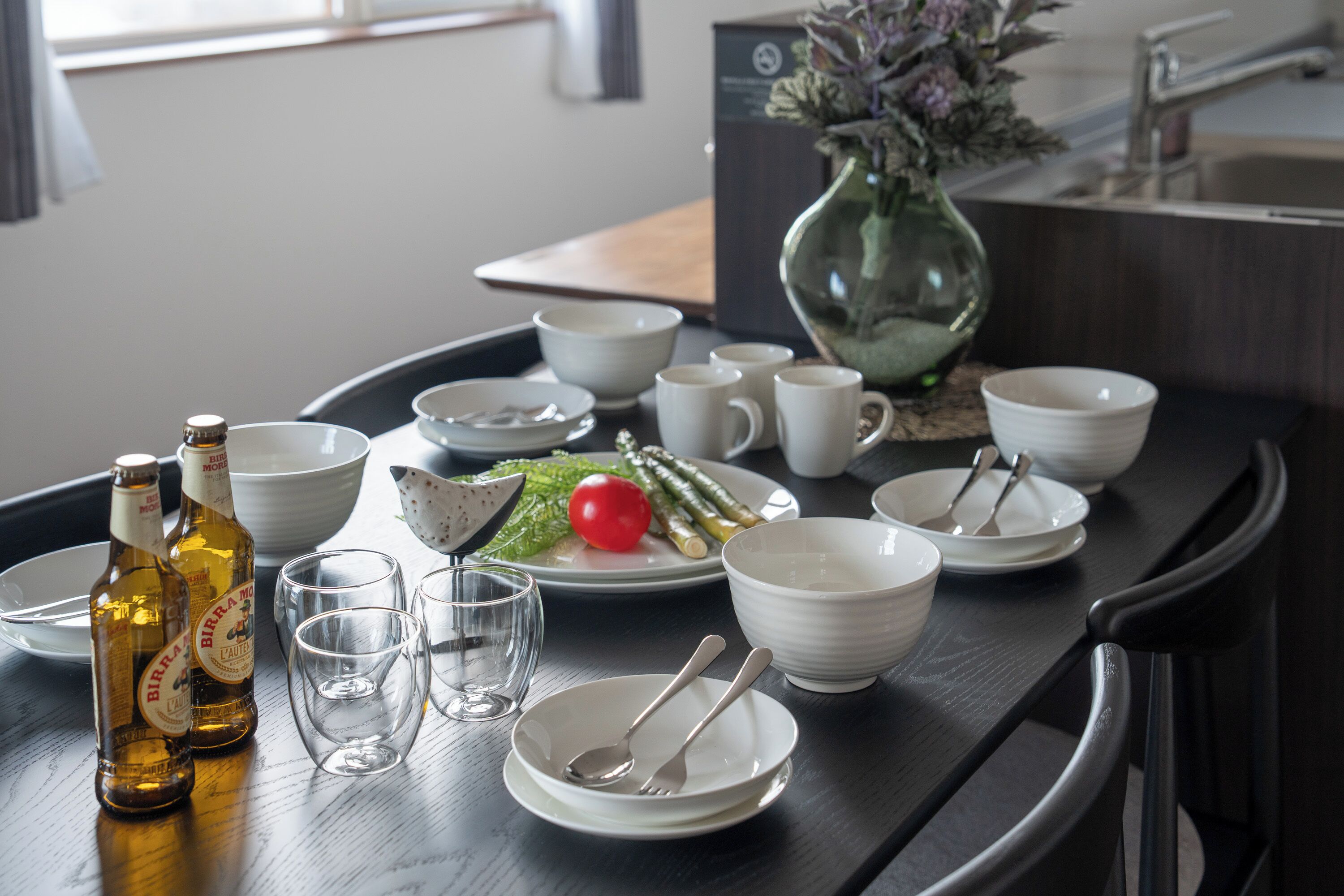 A dining table set with plates, bowls, glasses, and bottles, indicating a meal setup.