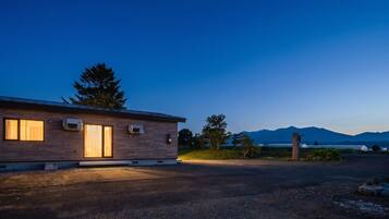 A modern house with a large window, an air conditioning unit, and a driveway leading to a gravel area.