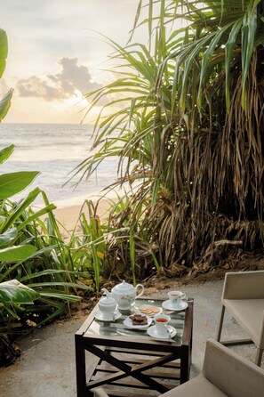 A table set with tea and cookies on a glass table near a beach, surrounded by plants. - Villa Sayura by TONIK, Galle (Boossa)