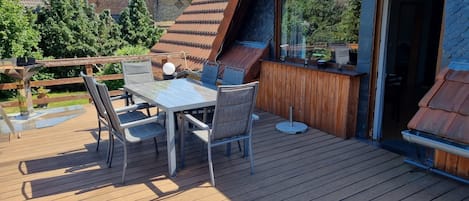 Eine Holzdar Terrasse mit Tisch und Stühlen, einem Tisch mit Glasplatte und Blick auf die Umgebung.