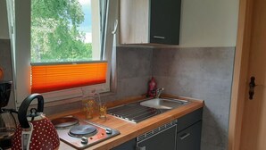 Eine Küche mit Holzarbeitsplatte, einem Wasserkocher, einer Spüle und einem Fenster mit Jalousien.