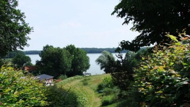 Ein Weg, der zu einem See führt, mit einem Haus im Hintergrund.