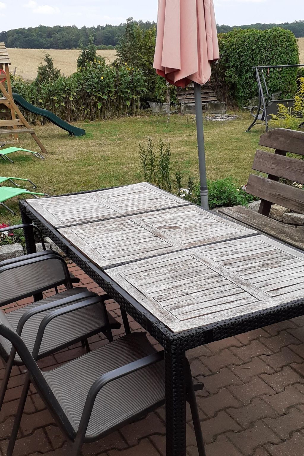 Un patio con mesa y sillas, rodeado de un jardín y un parque infantil.