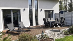 Een modern huis met een patio, een tafel en stoelen, een kleine tuin en een omheinde achtertuin.