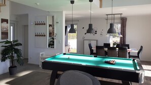 Een moderne woonkamer met een pooltafel, een eethoek en een trap.