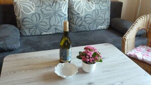 Een houten tafel met een fles wijn, een witte schaal in de vorm van een schelp en een kleine witte pot met roze bloemen.