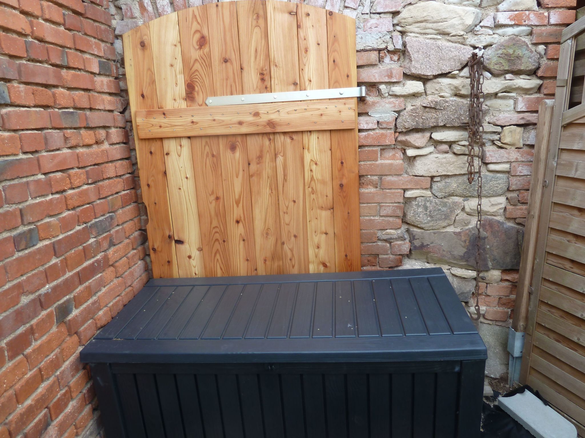 Uma porta de madeira com dobradiças de metal, uma parede de pedra e uma plataforma preta.