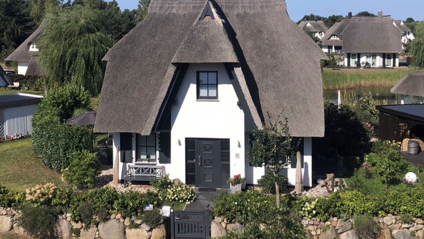 A house with a steeply pitched thatched roof, white walls, and a black front door. - Reetdachhaus am Wasser mit Sauna, Außenwhirlpool by Interhome (Bodstedt)