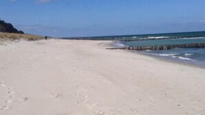 A wide sandy beach with footprints leading towards the water, a wooden pier extending into the sea, and a clear blue sky. - Reetdachhaus am Wasser mit Sauna, Außenwhirlpool by Interhome (Bodstedt)