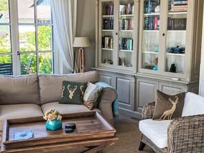 A living room with a sofa, a coffee table, a wicker chair, and a glass cabinet with books. - Reetdachhaus am Wasser mit Sauna, Außenwhirlpool by Interhome (Bodstedt)