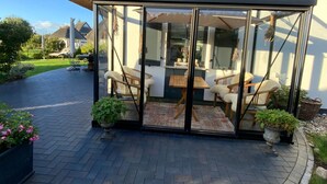 A conservatory with a glass door, a wooden table, and four chairs. - Reetdachhaus am Wasser mit Sauna, Außenwhirlpool by Interhome (Bodstedt)