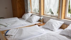 Ein Zimmer mit zwei Einzelbetten, Holzkopfteilen, weißer Bettwäsche und einem Fenster mit durchsichtigen Vorhängen.