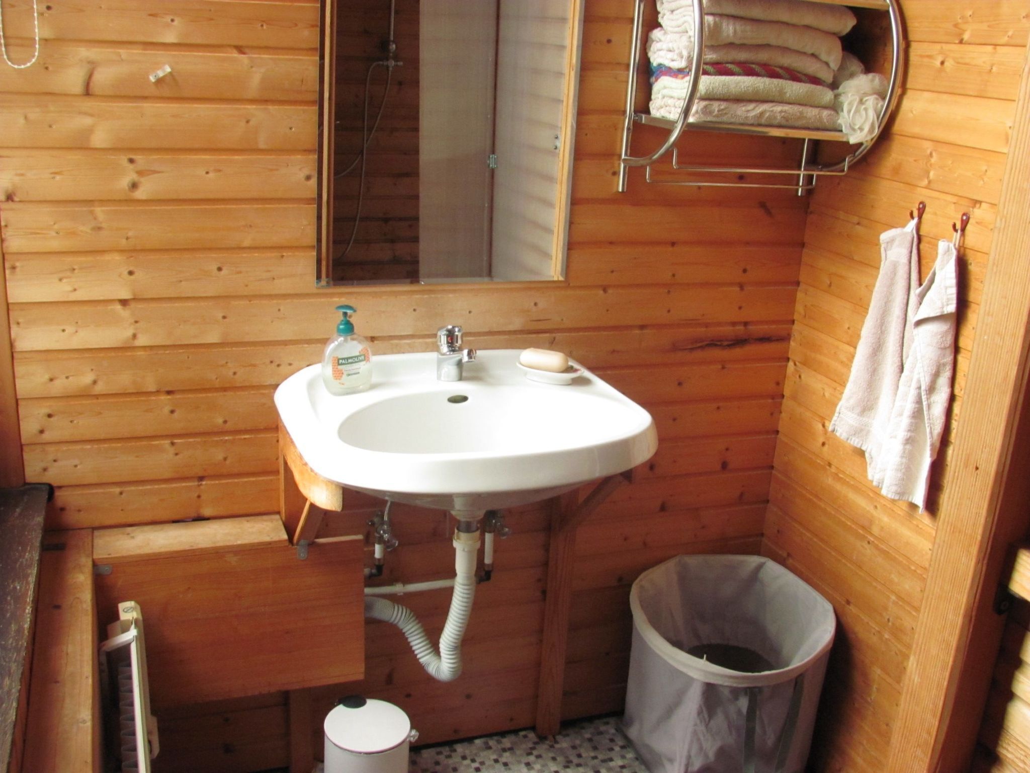 Bagno di una baita in legno con lavandino bianco, uno specchio, portasci e un cestino.