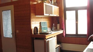 A compact kitchen with wooden walls, a refrigerator, a sink, and a window with curtains.